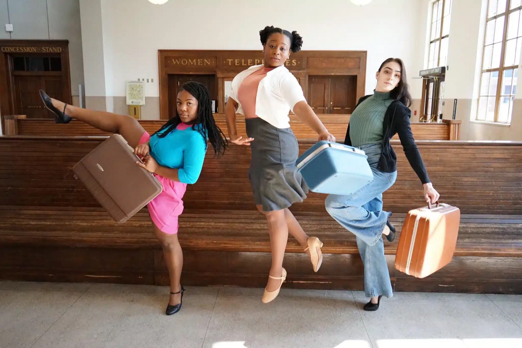 Three performers posing with suitcases in a station lobby